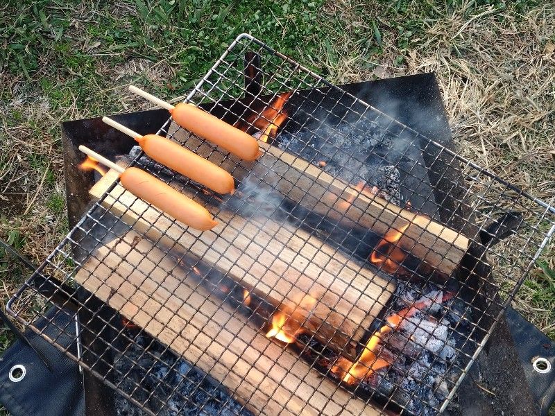 たき火で串付きフランクフルトを焼いている様子