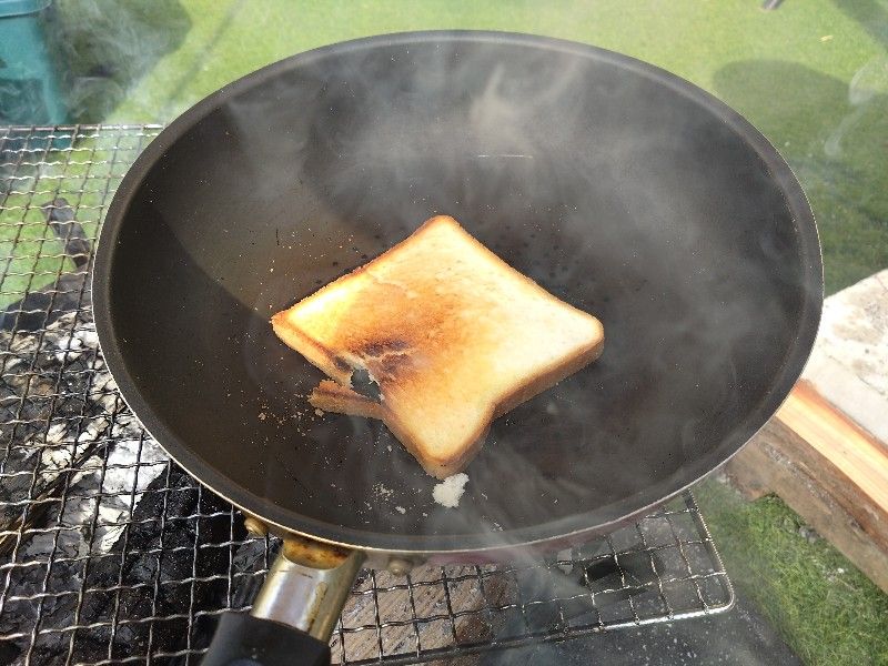 薪に火をつけ網の上にフライパンを置き食パンを焼いている