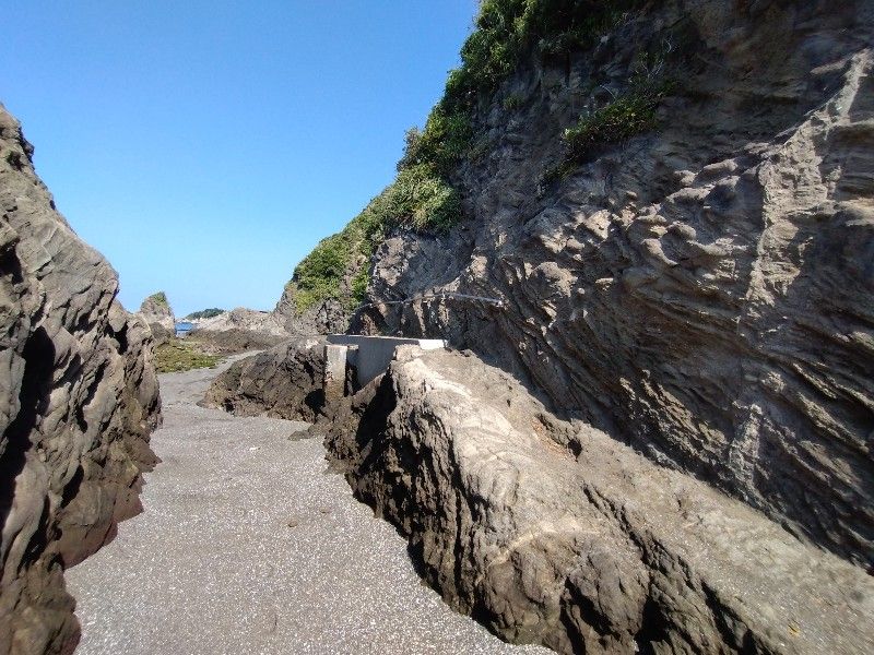 岩と岸壁に挟まれ細くなった砂浜の通路