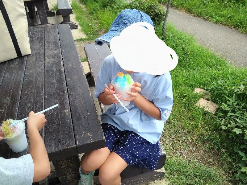 かき氷を食べるこども。水色、黄色、ピンクのシロップをかけた